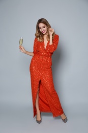 Photo of Happy woman in shiny dress with glass of champagne on grey background. Christmas party