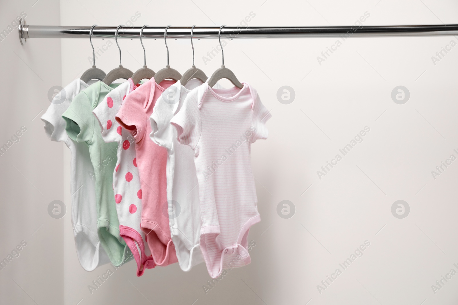 Photo of Baby bodysuits hanging on rack near white wall. Space for text