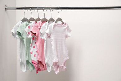 Baby bodysuits hanging on rack near white wall. Space for text