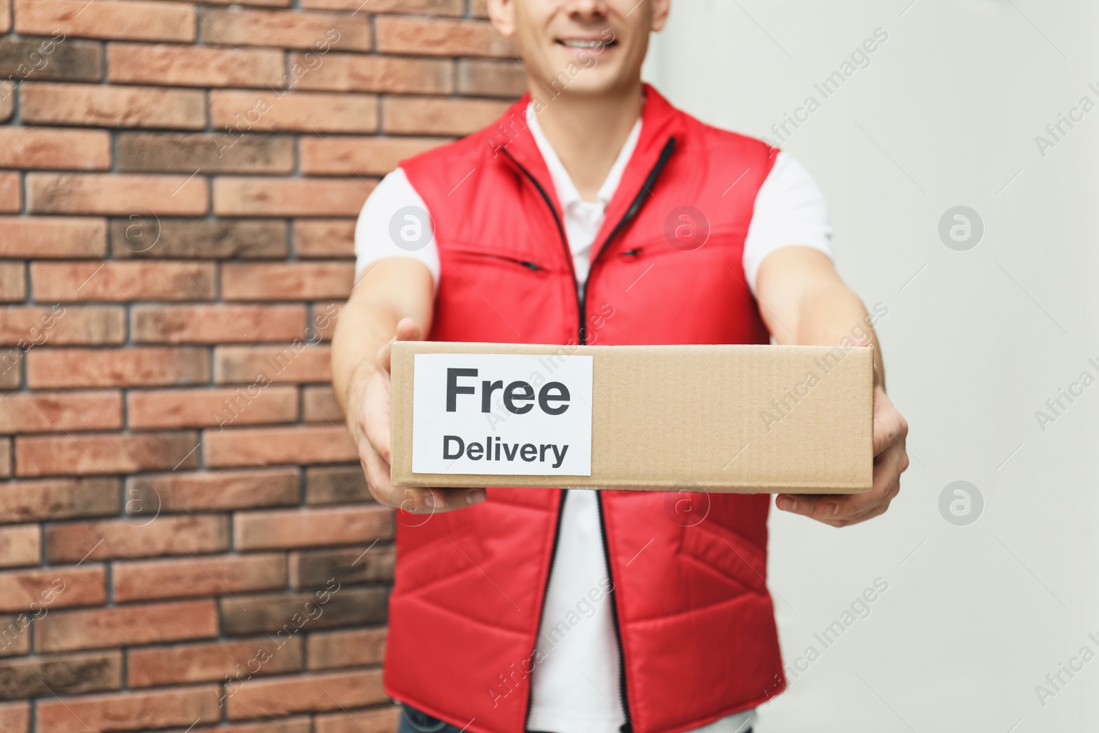 Photo of Courier holding parcel with sticker Free Delivery indoors, closeup