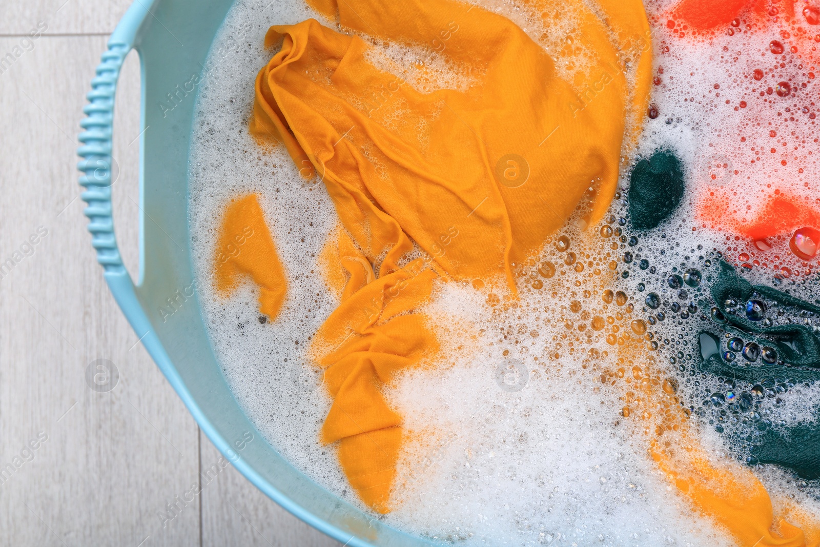 Photo of Basin with colorful clothes in suds on floor, top view. Hand washing laundry