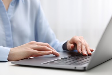 Photo of E-learning. Woman using laptop at white table indoors, closeup