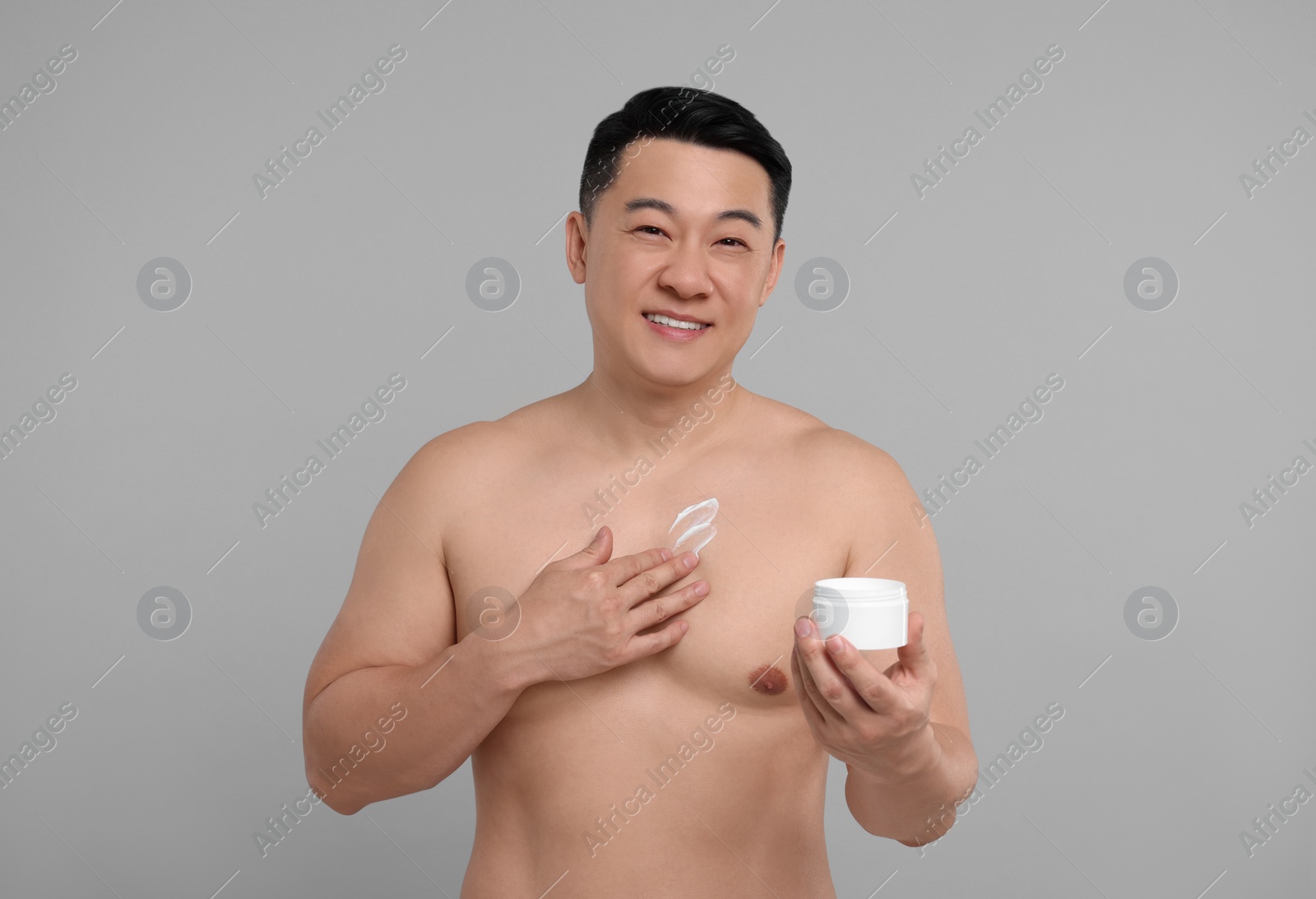 Photo of Handsome man with jar of body cream on light grey background