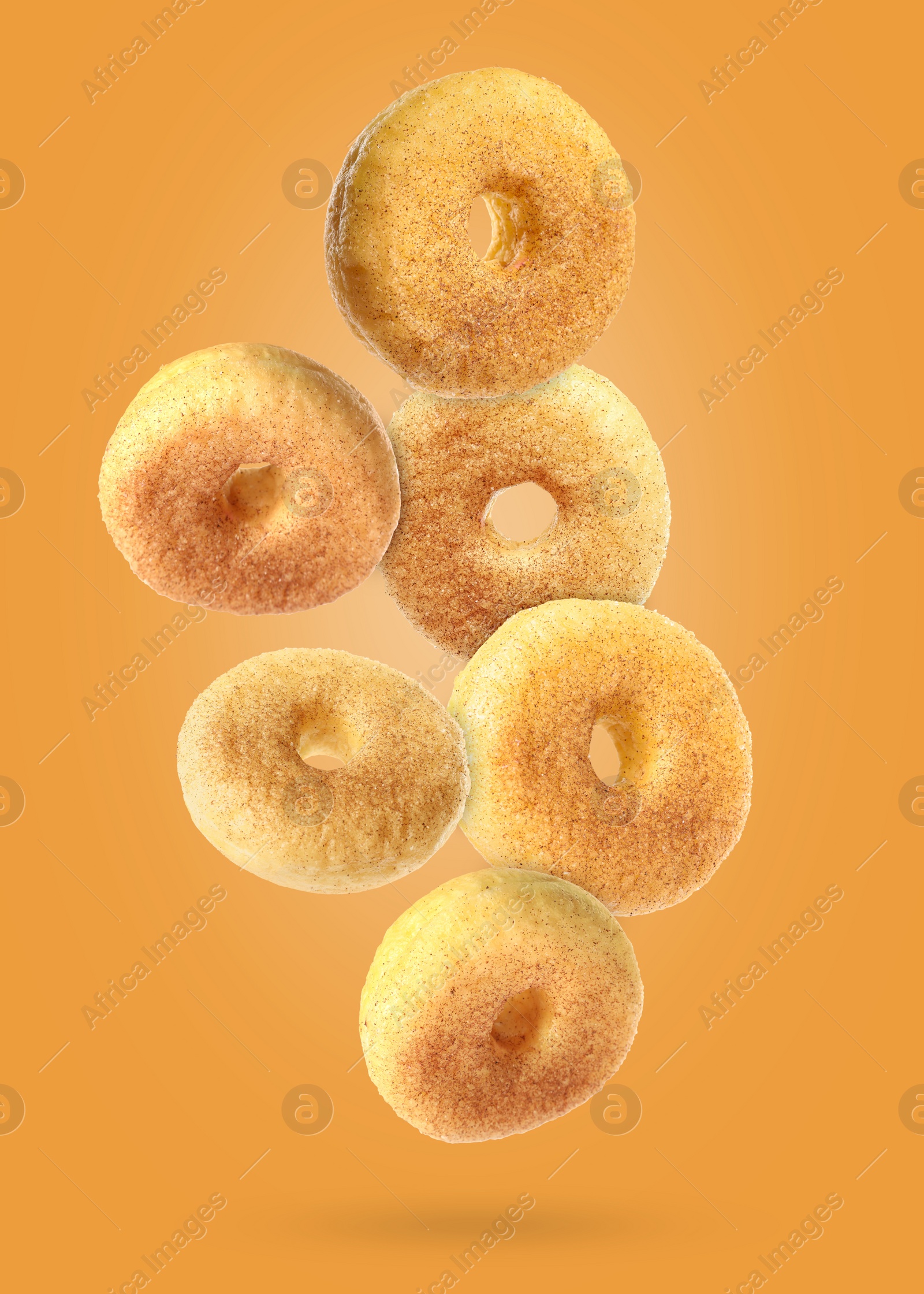 Image of Many sweet tasty donuts with cinnamon powder falling on orange background