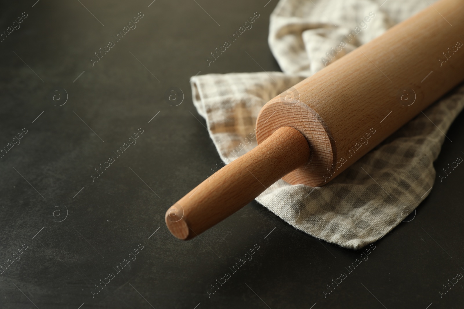 Photo of Rolling pin and kitchen towel on black table, closeup. Space for text