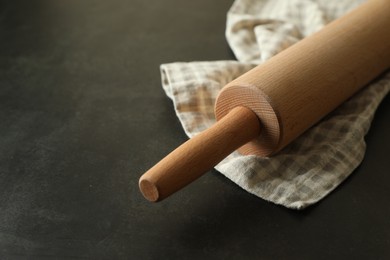 Photo of Rolling pin and kitchen towel on black table, closeup. Space for text