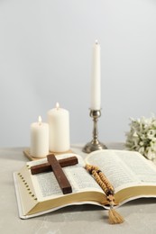 Photo of Church candles, wooden cross, rosary beads, Bible and flowers on light table