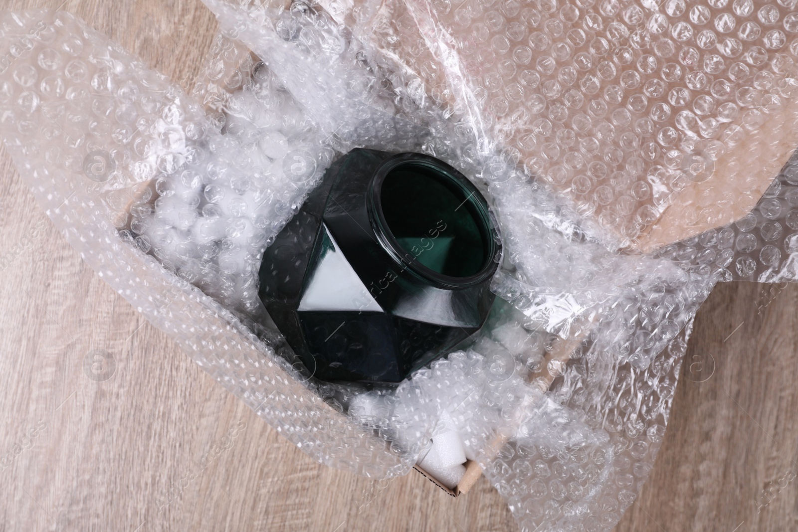 Photo of Glass vase with bubble wrap and packaging foam in cardboard box on wooden table, top view