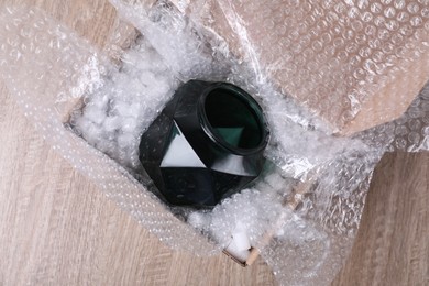 Glass vase with bubble wrap and packaging foam in cardboard box on wooden table, top view