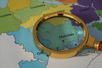 Golden magnifying glass above Mykolaiv region on map of Ukraine, closeup