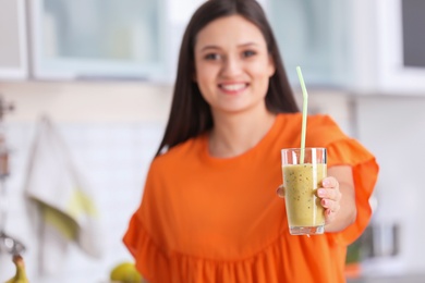 Young woman with glass of tasty healthy smoothie in kitchen