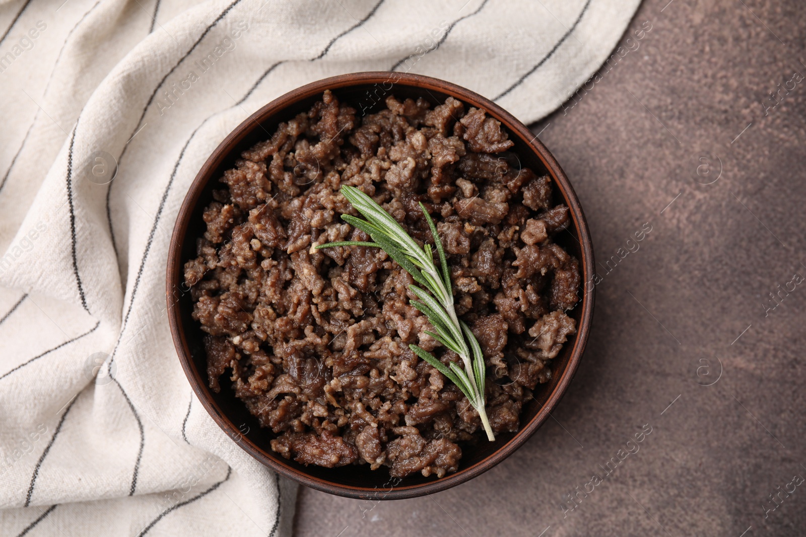 Photo of Fried ground meat in bowl and rosemary on brown textured table, top view