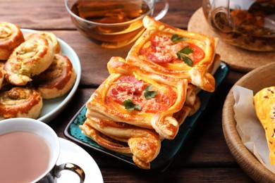 Photo of Various delicious puff pastry served with tea on wooden table