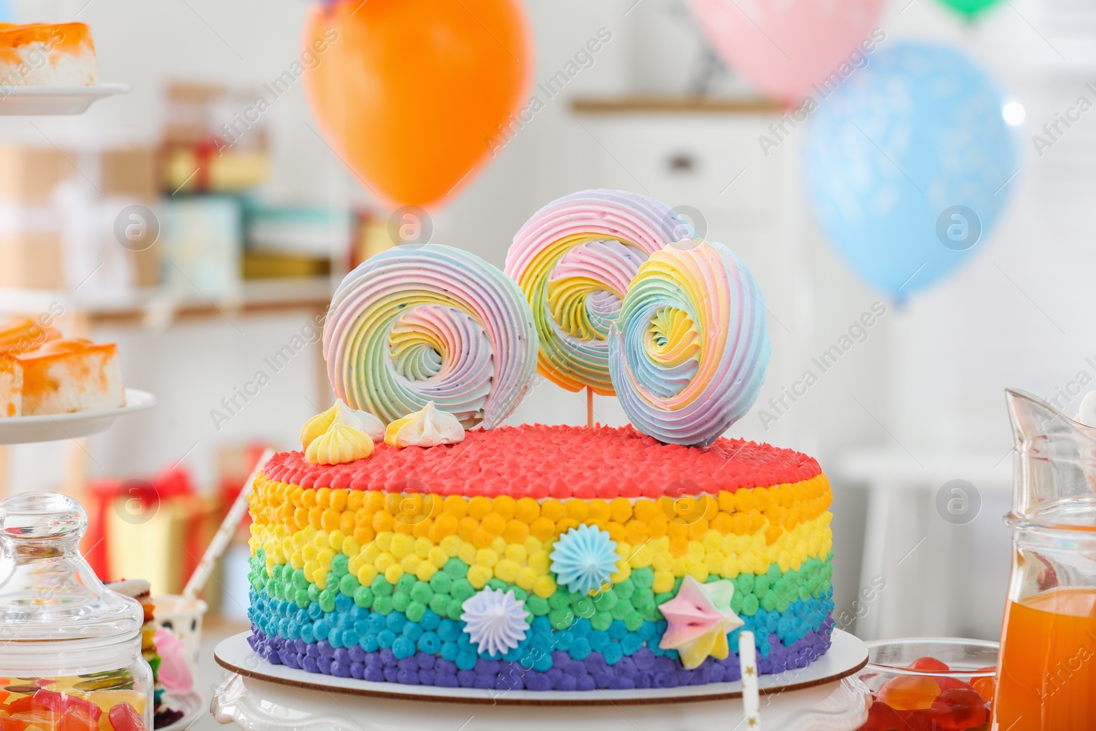 Photo of Bright birthday cake and other treats on table in decorated room