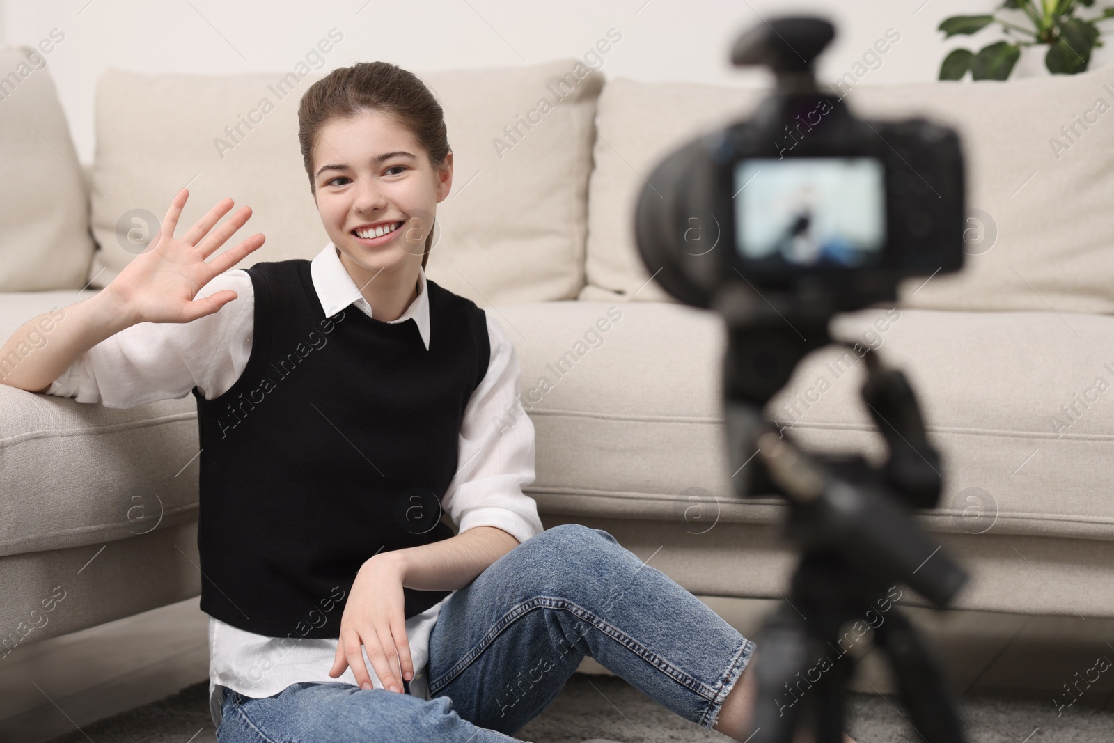 Photo of Smiling teenage blogger waving hello to her subscribers while streaming at home