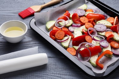 Baking pan with parchment paper and raw vegetables on grey wooden table