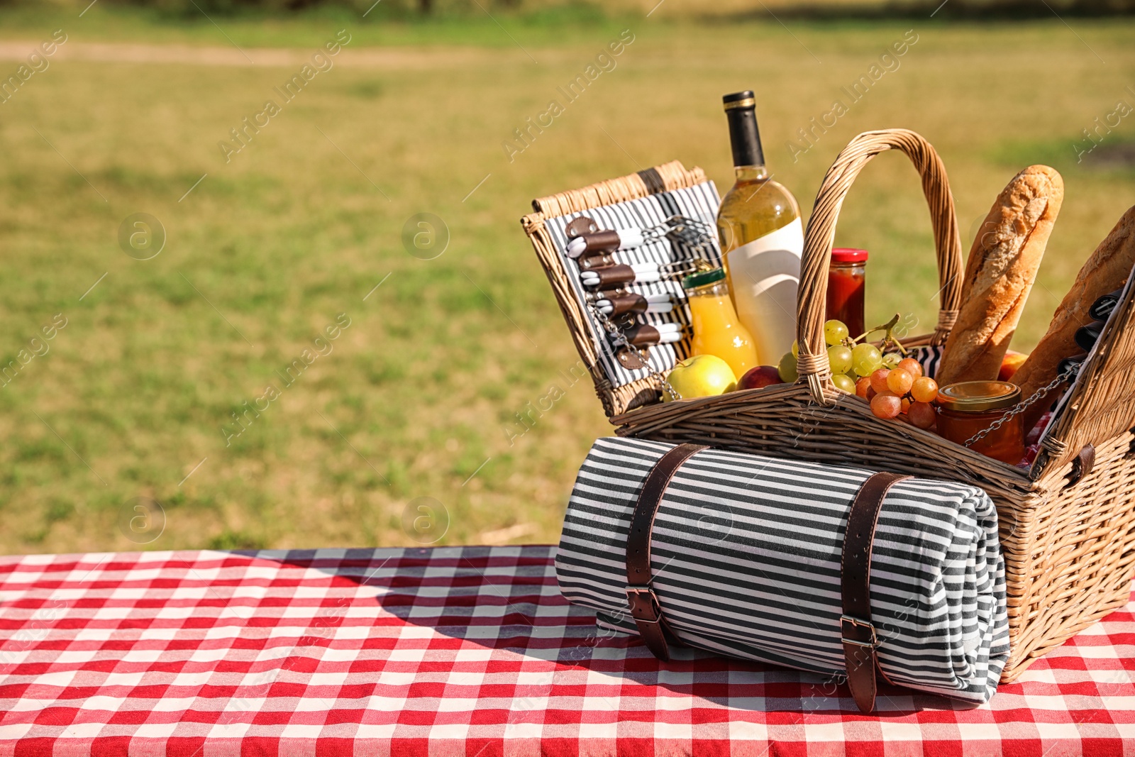 Photo of Picnic basket with wine, snacks and mat on table in park. Space for text