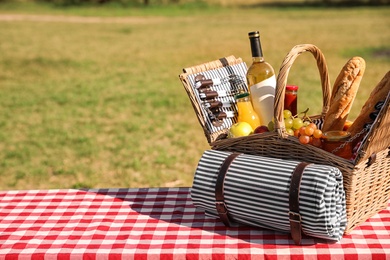 Picnic basket with wine, snacks and mat on table in park. Space for text