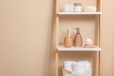 Different bath accessories and personal care products on shelving unit near beige wall, space for text