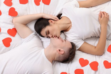 Photo of Lovely couple kissing on bed with many decorative hearts, top view. Valentine's day celebration