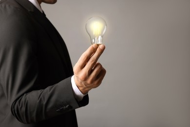 Photo of Glow up your ideas. Closeup view of businessman holding light bulb on grey background, space for text