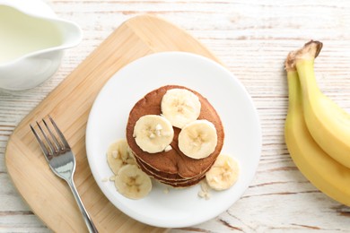 Photo of Plate of banana pancakes served on white wooden table, flat lay
