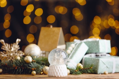 Photo of Beautiful snow globe, gifts and Christmas decor on wooden table against blurred festive lights