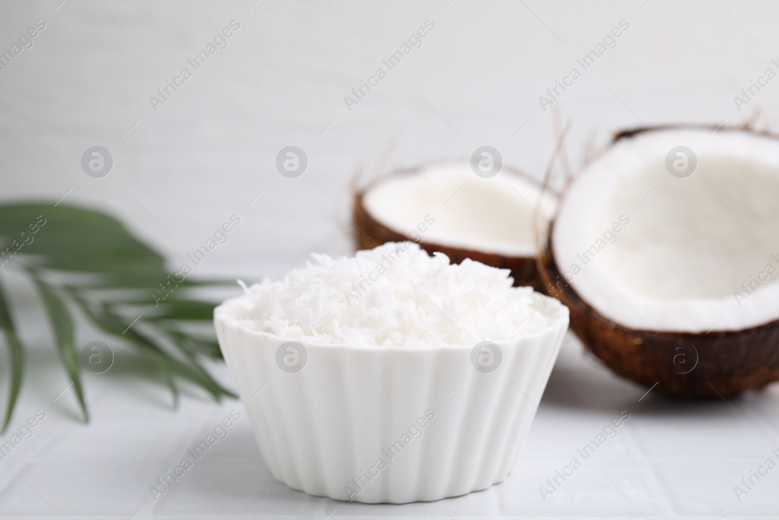 Photo of Coconut flakes in bowl, nuts and palm leaf on white tiled table