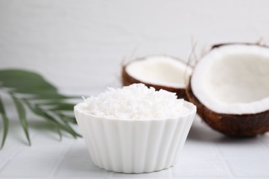 Coconut flakes in bowl, nuts and palm leaf on white tiled table