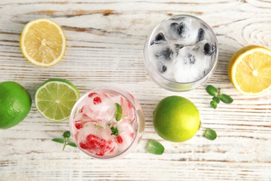 Photo of Glasses of drinks with ice cubes and fruits on wooden background, flat lay