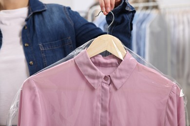 Photo of Dry-cleaning service. Woman holding shirt in plastic bag indoors, closeup