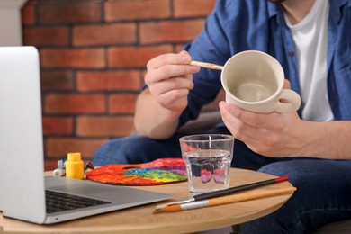 Man learning to decorate cup while watching online course indoors, closeup. Time for hobby