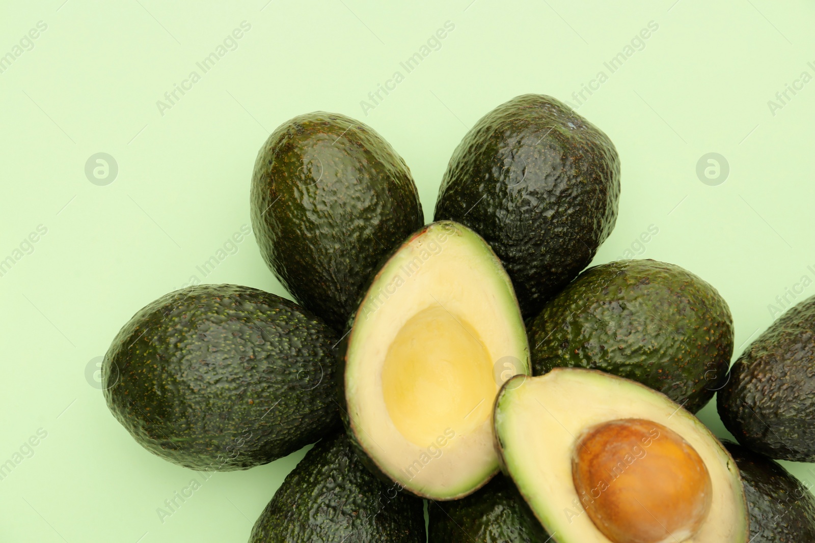 Photo of Tasty whole and cut avocados on light green background, flat lay