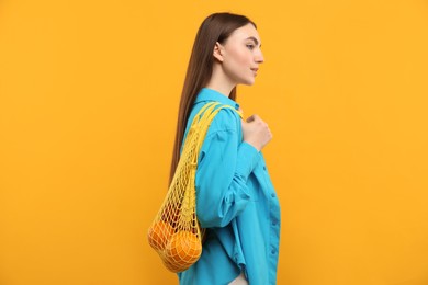 Photo of Woman with string bag of fresh oranges on orange background