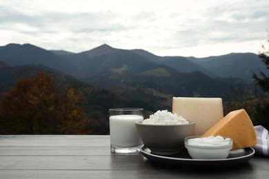 Photo of Tasty cottage cheese and other fresh dairy products on grey wooden table in mountains. Space for text