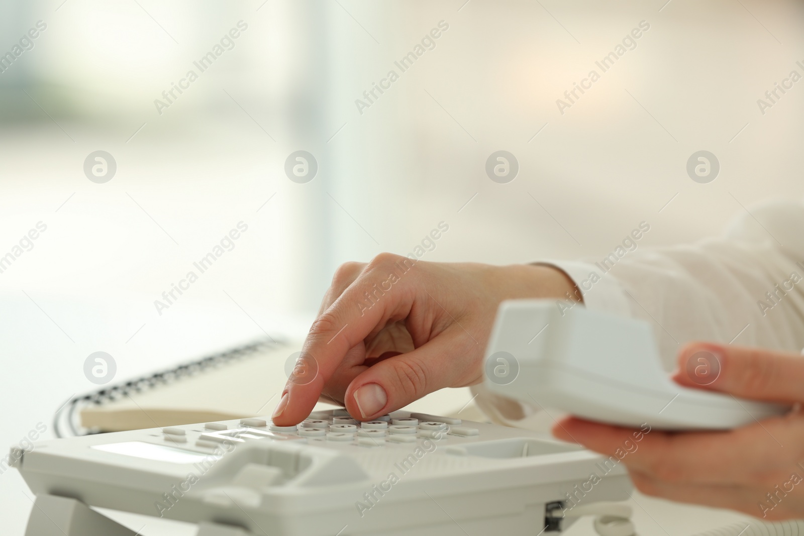 Photo of Assistant dialing number on telephone against blurred background, closeup