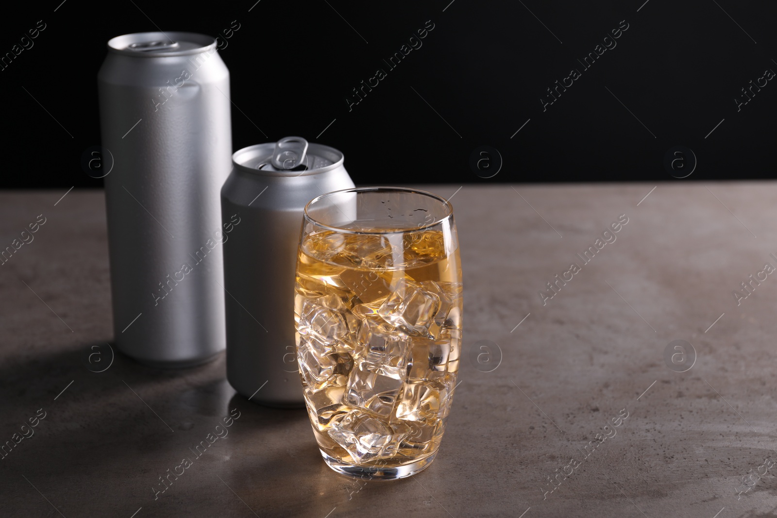 Photo of Energy drink with ice cubes in glass and aluminium cans on grey table. Space for text