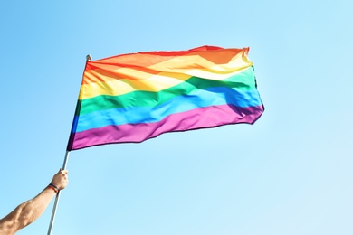 Photo of Gay man holding rainbow LGBT flag on blue sky background