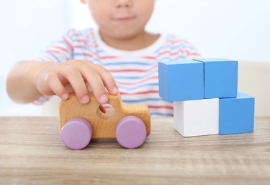 Photo of Little boy playing with toys at wooden table, closeup