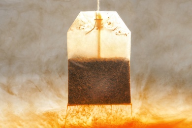 Photo of Brewing tea with bag in hot water, closeup