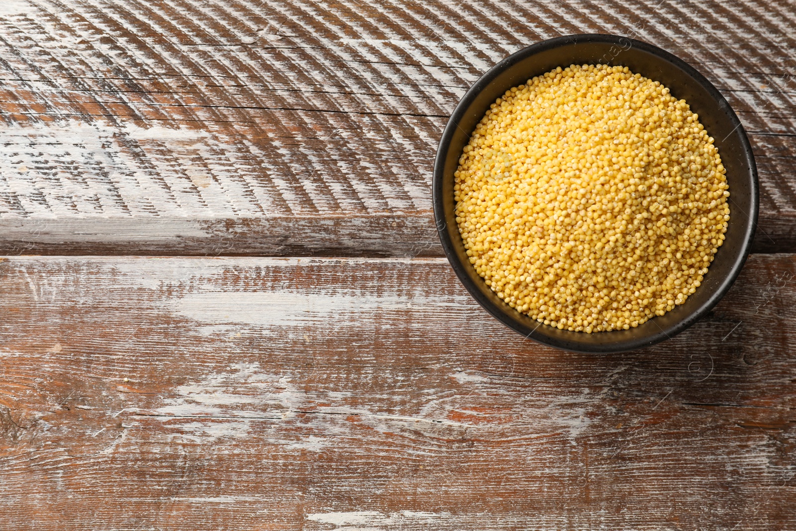 Photo of Millet groats in bowl on wooden table, top view. Space for text