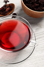 Photo of Cup of fresh hibiscus tea and dry flower leaves on wooden table, above view