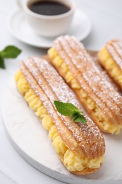 Photo of Delicious eclairs filled with cream and mint on white table