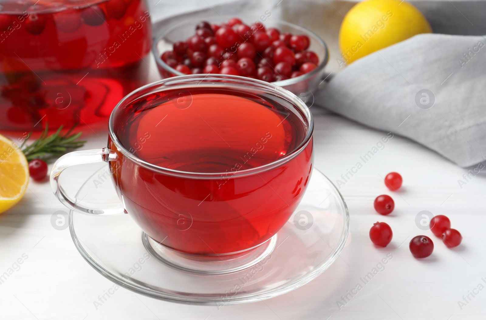 Photo of Tasty hot cranberry tea in glass cup and fresh berries on white table