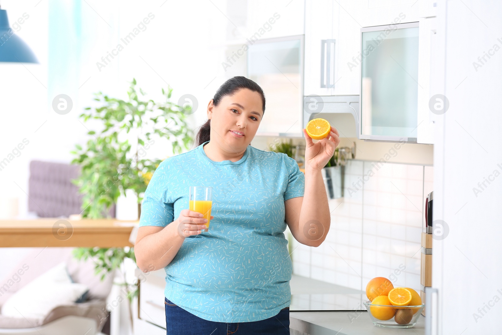 Photo of Overweight woman with glass of fresh juice and orange in kitchen. Healthy diet