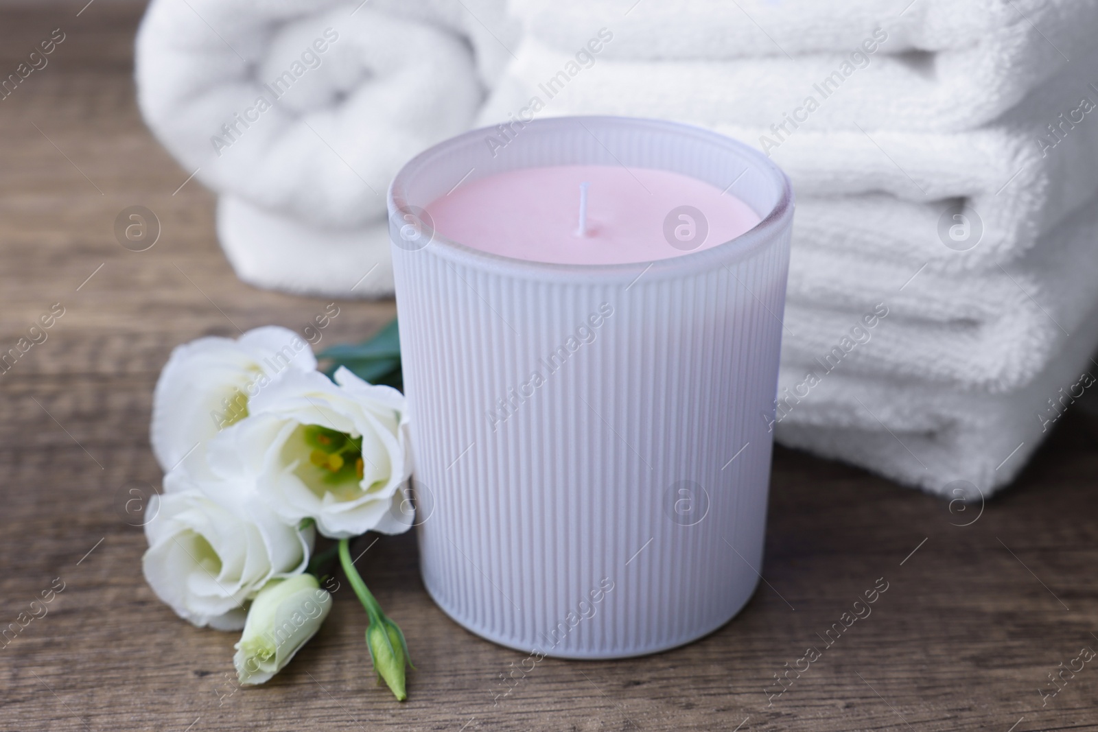 Photo of Scented candle, folded towels and eustoma flowers on wooden table