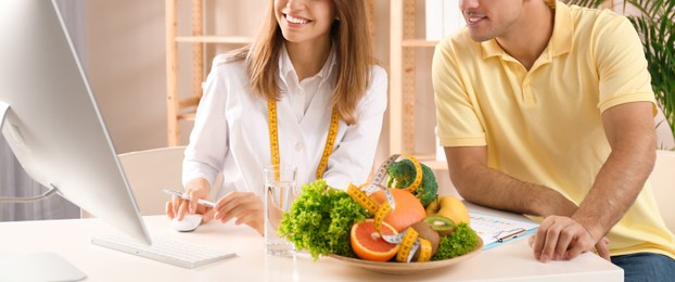 Image of Young nutritionist consulting patient at table in clinic, closeup. Banner design