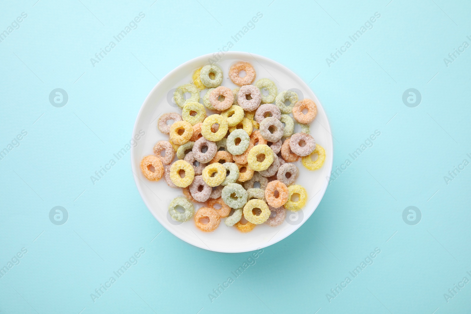 Photo of Tasty colorful cereal rings and milk in bowl on turquoise background, top view