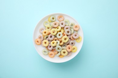 Tasty colorful cereal rings and milk in bowl on turquoise background, top view