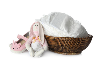 Photo of Wicker bowl with disposable diapers, child's shoes and toy bunny on white background